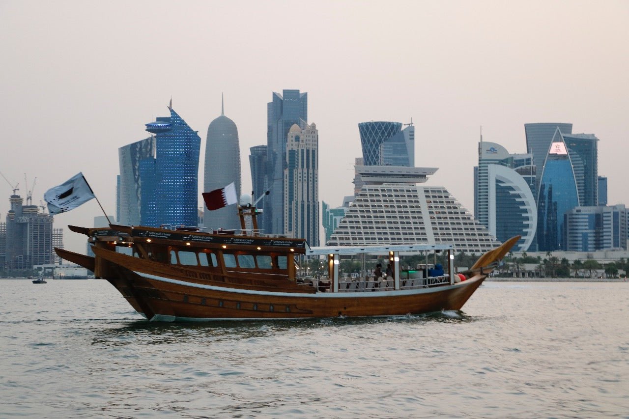 Traditional dhow sailing in front of the Doha West Bay skyline at sunset
